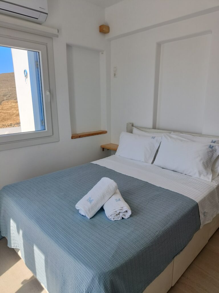Elegant en‑suite double bedroom with upholstered headboard, warm lighting and balcony access at Villa Manesi in Kythnos