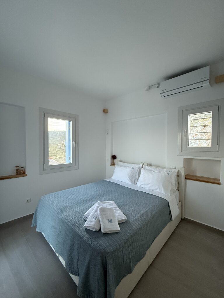 Elegant en-suite double bedroom with soft lighting and private balcony at Villa Manesi, Kythnos